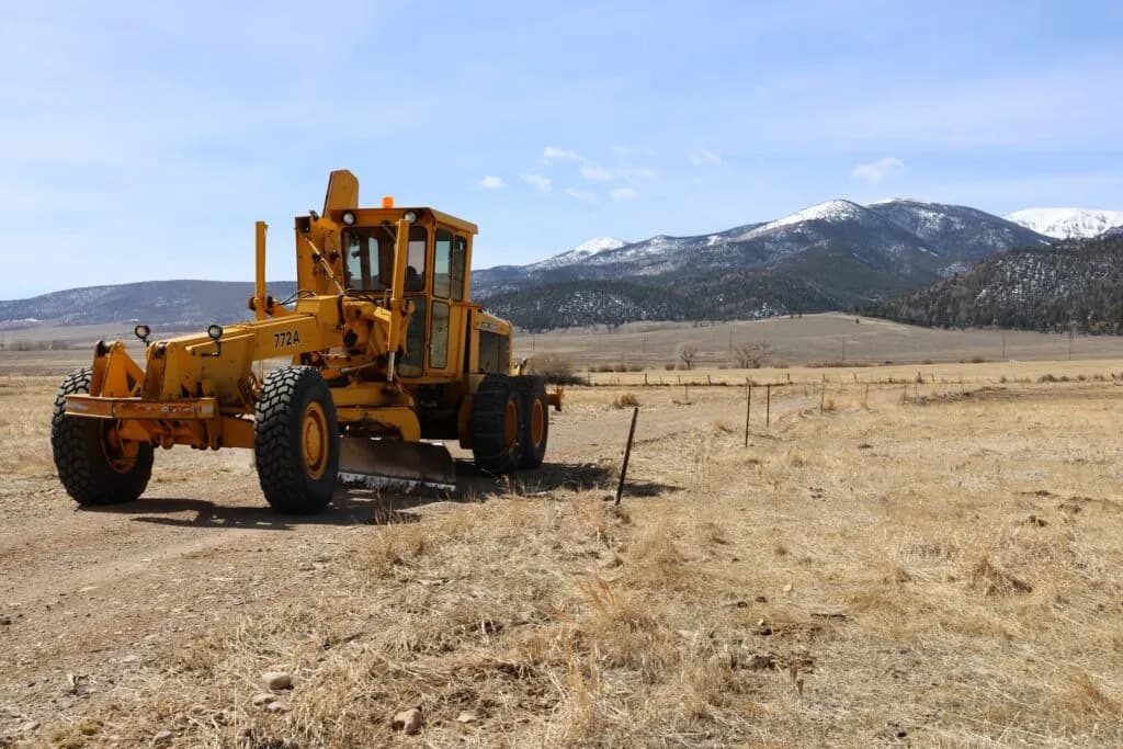 4RE | A John Deere motor grader with the Rocky Mountains in the background.